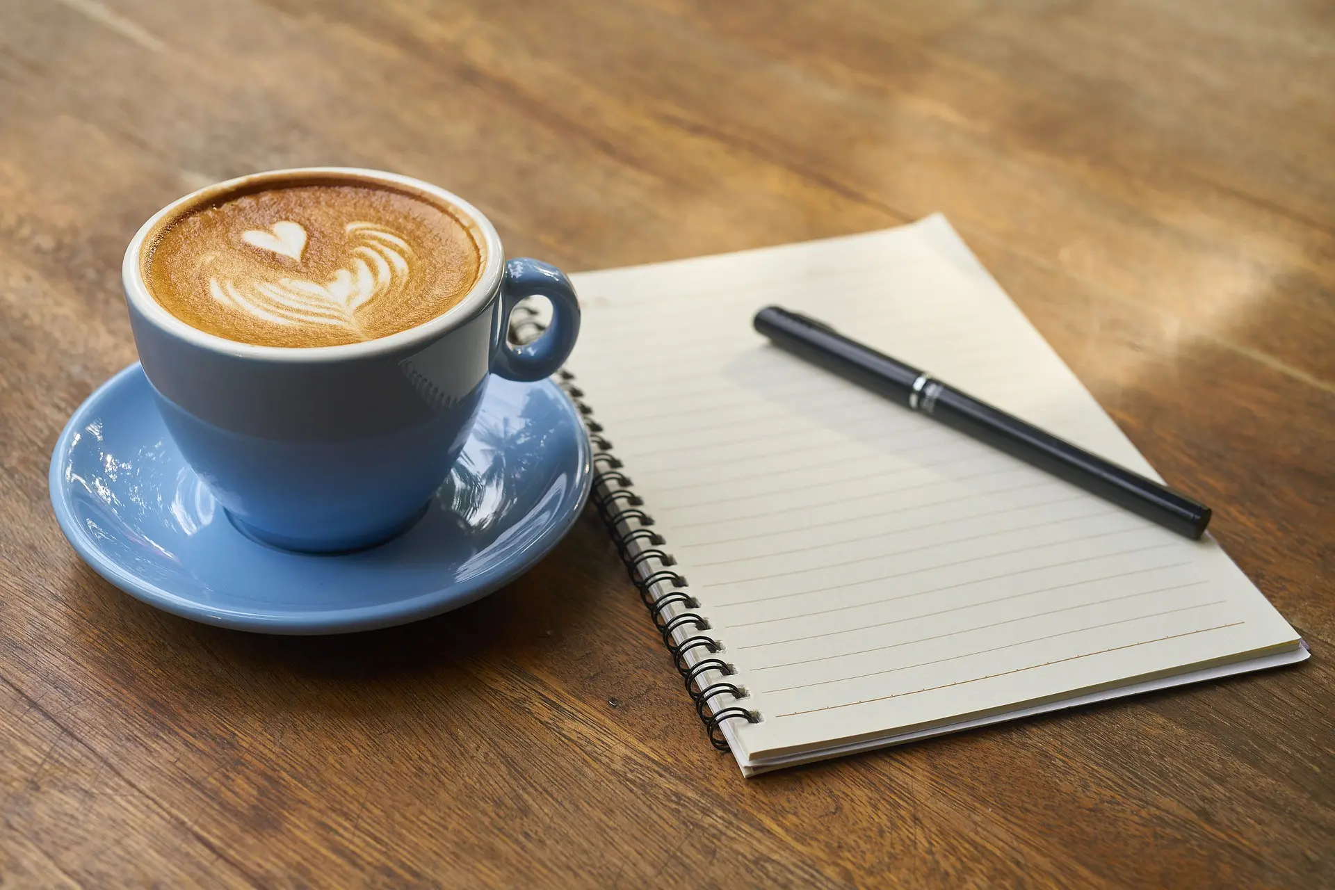 Notebook and pen beside a cup of coffee